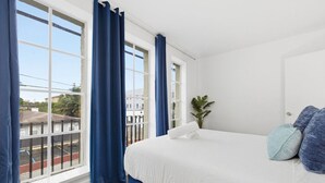 A bedroom with a large bed, white walls, and a view of the street through a window with blue curtains. - Large 2BR Luxury Flat - Near Brickell City Center (Miami)