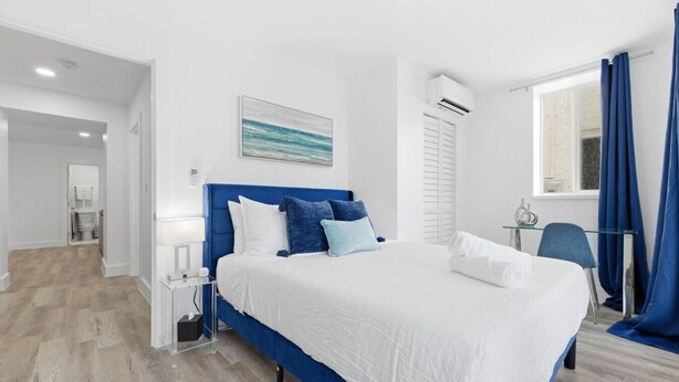 A modern bedroom with a large bed, a bedside table, a desk, and a window with curtains. - Large 2BR Luxury Flat - Near Brickell City Center (Miami)
