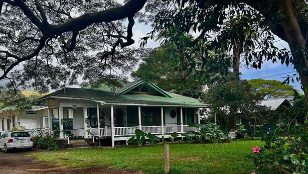 A two-story house with a green roof, a porch, and a car parked in front. - Hale Naalehu LLC Bed & Breakfast (Naalehu)