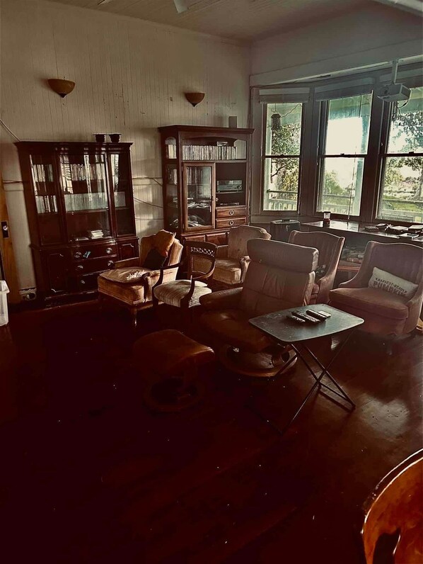 Ein geräumiges Wohnzimmer mit einer großen Holzkassette, mehreren Sesseln, einem Couchtisch und Blick durch große Fenster.
