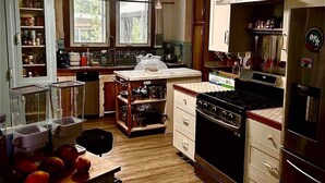 A kitchen with wooden cabinets, a stove, a refrigerator, and a window. - Hale Naalehu LLC Bed & Breakfast (Naalehu)