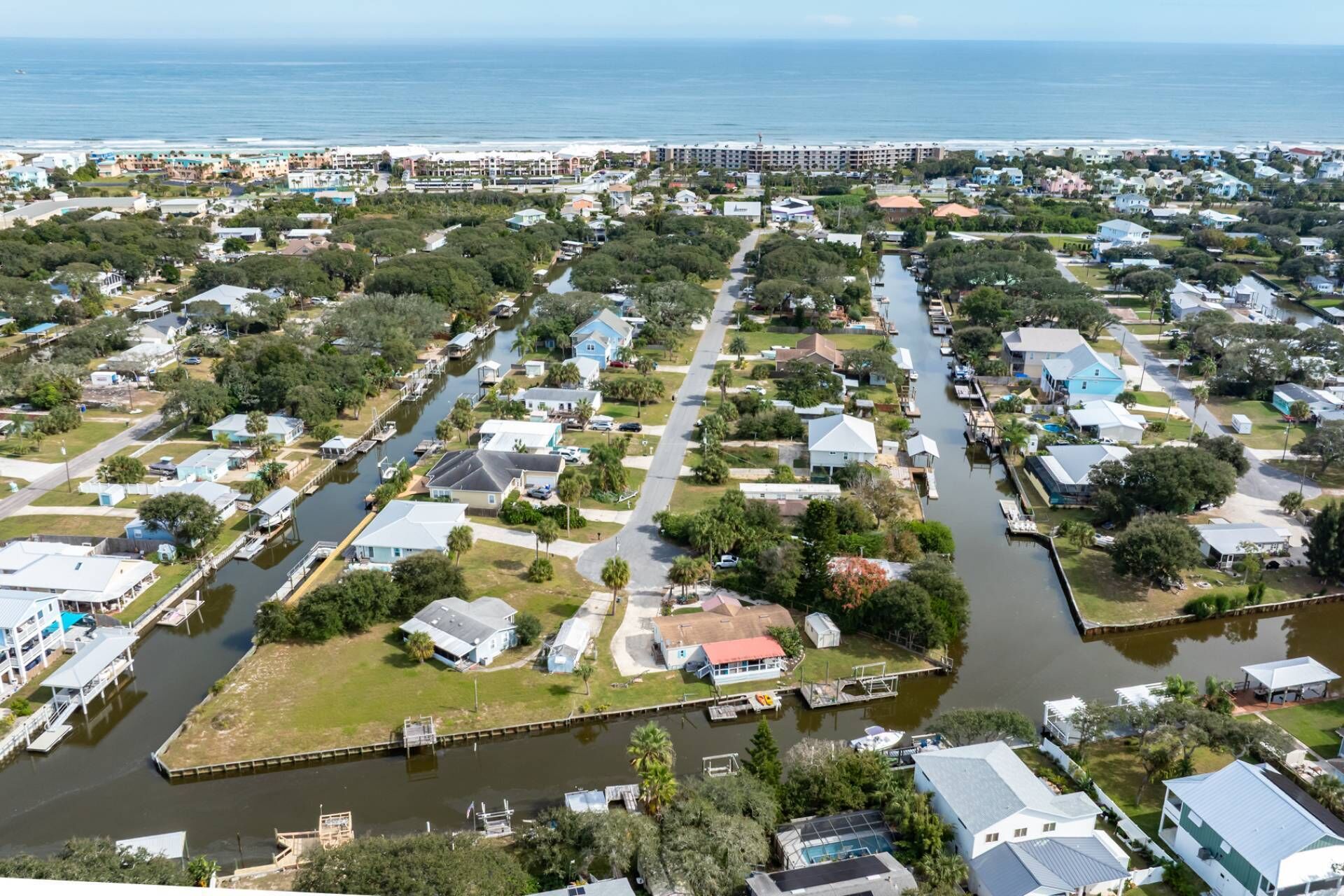 An aerial view of a residential area with houses, a canal, and a beach in the background.