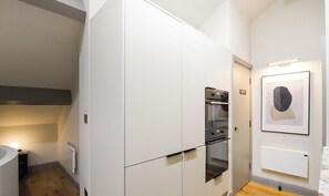 A modern kitchen with built-in appliances, a white cabinetry design, and a framed artwork on the wall. - Brooklyn | The Heim (Greater Manchester)