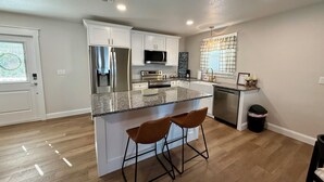A modern kitchen with white cabinets, stainless steel appliances, and a granite countertop. There are two bar stools at the island. - Lakefront oasis offering breathtaking views & relaxation. Perfect for unwinding! (Avon Park)