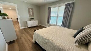 A bedroom with a large bed, a dresser, a ceiling fan, and a window with curtains. - Lakefront oasis offering breathtaking views & relaxation. Perfect for unwinding! (Avon Park)