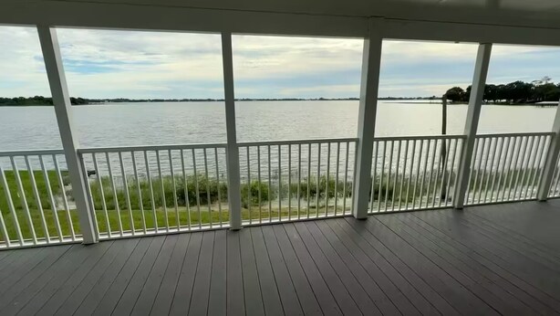 A covered deck with a view of a lake, white railings, and a grassy area in the foreground. - Lakefront oasis offering breathtaking views & relaxation. Perfect for unwinding! (Avon Park)