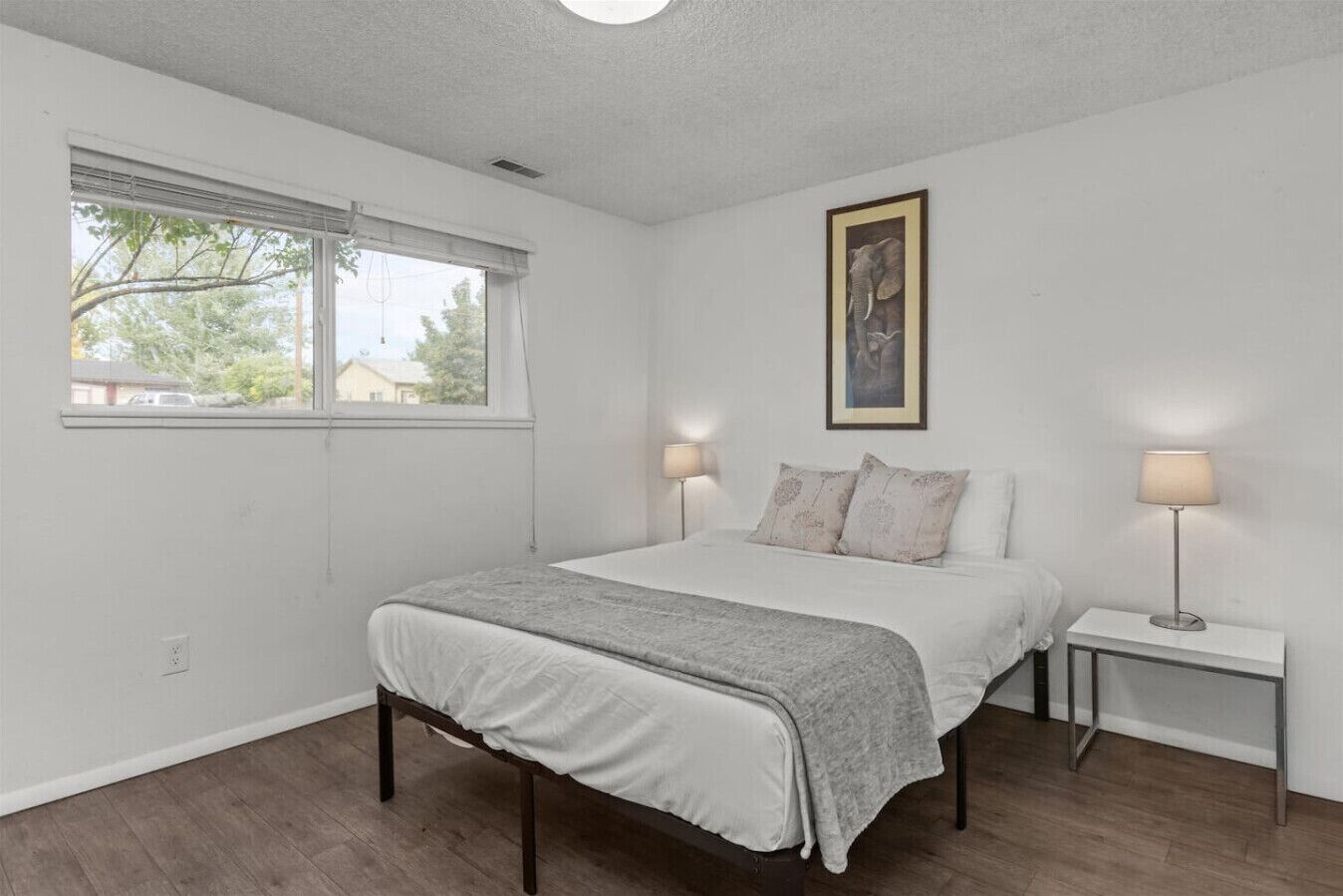 Une chambre à coucher avec un lit, deux tables de chevet, une fenêtre et un tableau au mur.