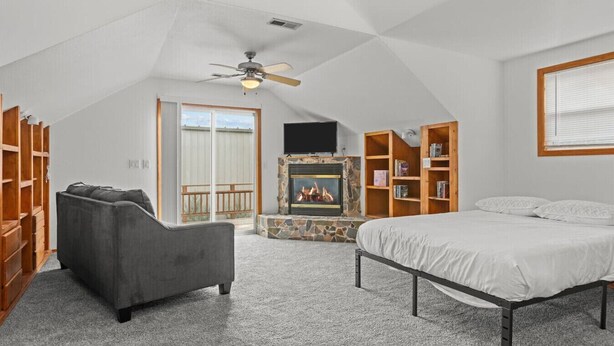 Um quarto de sótão amplo com lareira, uma cama, um sofá e estantes embutidas.