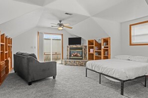 Un amplio dormitorio en el ático con chimenea, cama, sofá y estanterías empotradas.