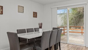 Uma área de refeições com uma mesa de mármore, cadeiras estofadas cinzas e um vaso branco com plantas.