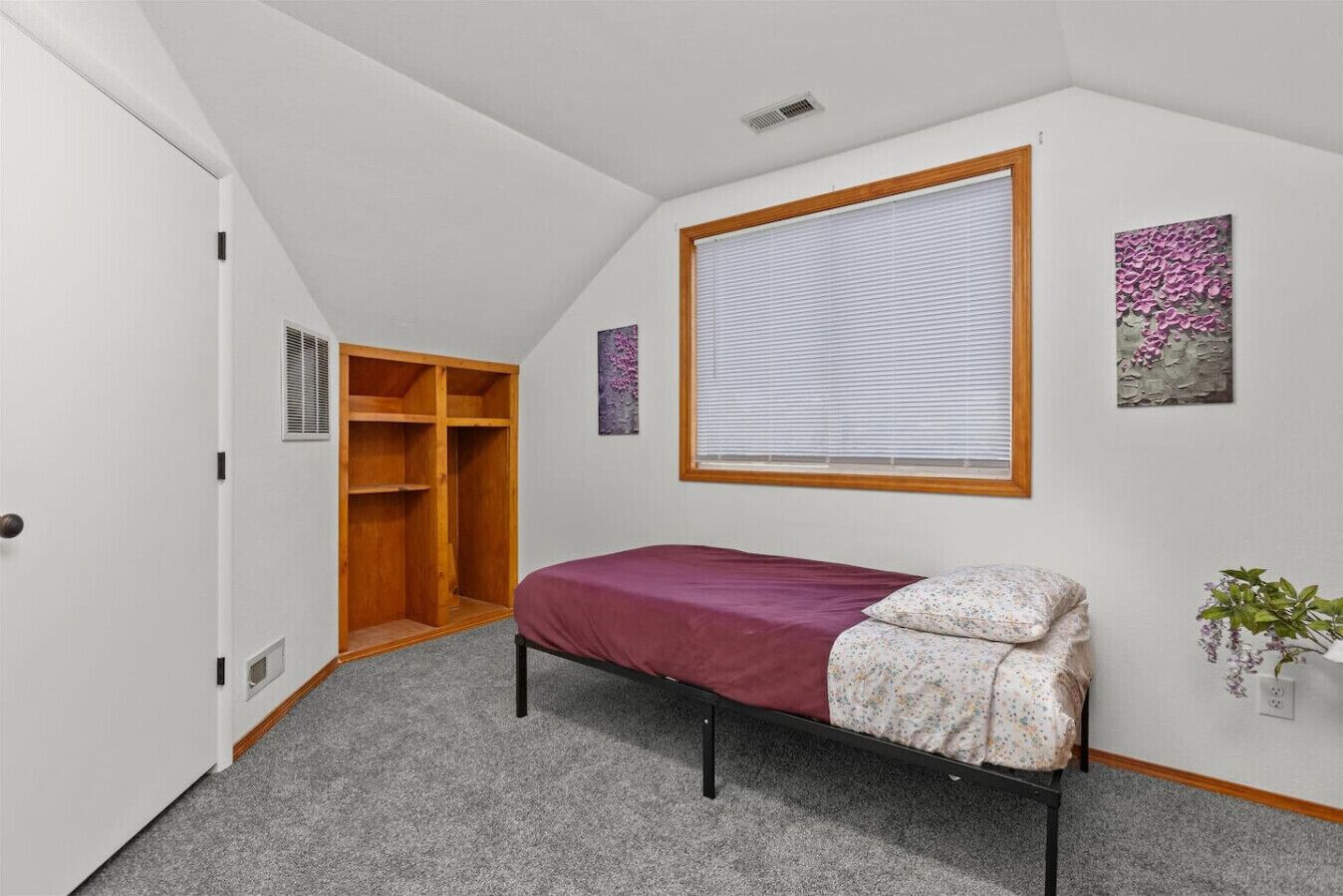 Ein Schlafzimmer mit einem Einzelbett, einem begehbaren Kleiderschrank, einem Fenster mit Jalousien und einer kleinen Pflanze an der Wand.