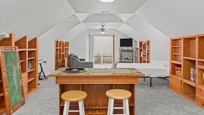Um quarto de sótão aconchegante com uma mesa de madeira, dois banquinhos, um ventilador de teto e uma lareira.