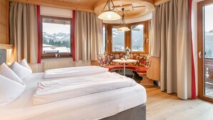A hotel room with a large bed, a round table with a chair, and a view of mountains through the windows. - 2 Apartments, Sauna & ski bus at the door (Wildschönau)