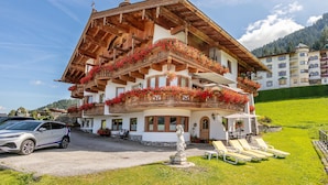 A traditional chalet with wooden balconies adorned with flowers, a statue in front, and a well-maintained lawn with sun loungers. - 2 Apartments, Sauna & ski bus at the door (Wildschönau)