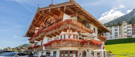 A traditional chalet with wooden balconies adorned with flowers, a statue in front, and a well-maintained lawn with sun loungers.