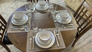 A round wooden dining table set for four with white plates, bowls, and clear glasses.