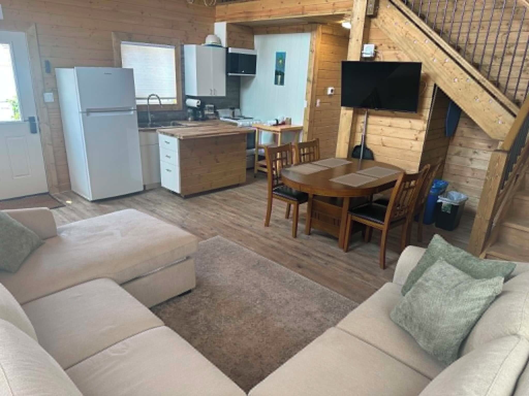 Espai habitable compacte amb zona de cuina americana, menjador i saló amb sofà i otomana.