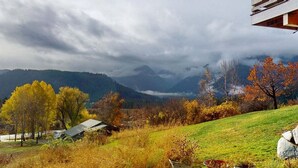 Ländliche Landschaft mit einem Haus auf einem Hügel, Herbstlaub und einem Berg im Hintergrund.