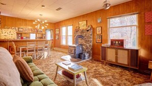 Ein gemütliches Wohnzimmer mit Kamin aus Stein, Holzwänden, einer Essecke und einer Küche.