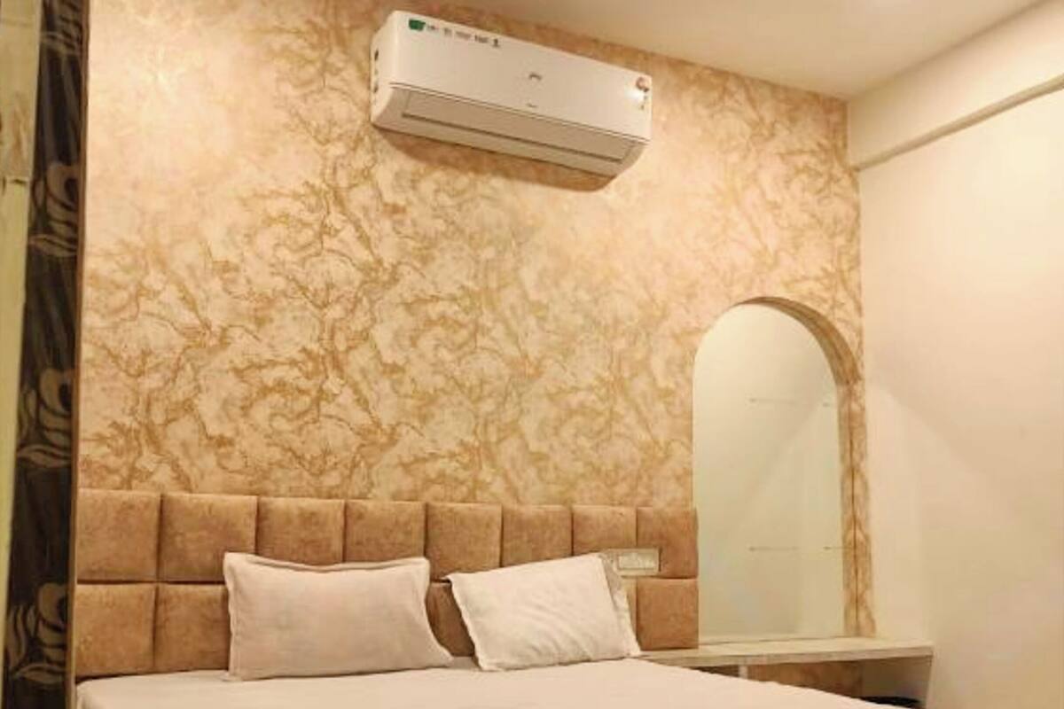 A bedroom with a marble-patterned wall, a tufted headboard, a bed with white bedding, a bedside table, and a wall-mounted air conditioning unit.