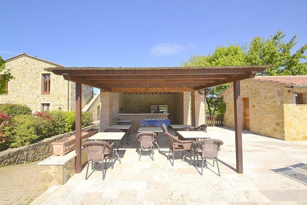 Une terrasse extérieure avec des tables en pierre et des chaises en osier, une pergola et un bâtiment en pierre en arrière-plan.