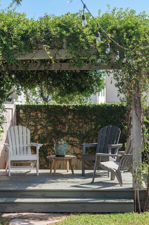 A wooden deck with two Adirondack chairs, a small round table, and a potted plant.