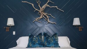 A bed with white linens and blue floral pillows, a wall-mounted tree branch decor, and two wall sconces with white lamps. - Sunflower Cottage | Cozy Autumn Escape (Pensacola)