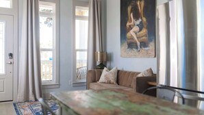 A living room with a beige sofa, a painting, a lamp, and a large window with curtains. - Sunflower Cottage | Cozy Autumn Escape (Pensacola)
