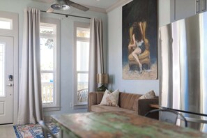 A living room with a beige sofa, a painting, a lamp, and a large window with curtains. - Sunflower Cottage Downtown (Pensacola)