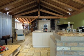 Une cuisine rustique avec une cheminée en pierre, des poutres en bois et un îlot central doté d’un évier.