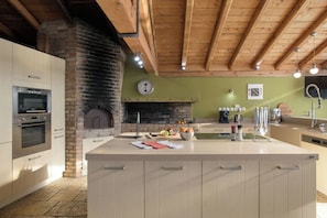 A kitchen with a brick oven, stainless steel appliances, and a wooden ceiling.