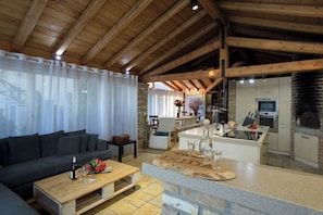 A cozy living area with a sofa, coffee table, and a kitchen with a brick oven. - Villa Irida by PosarelliVillas (Acharavi)