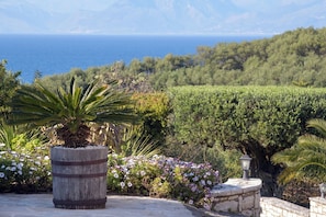 Un giardino curato con un vaso a botte in legno, piante fiorite e vista sul mare.