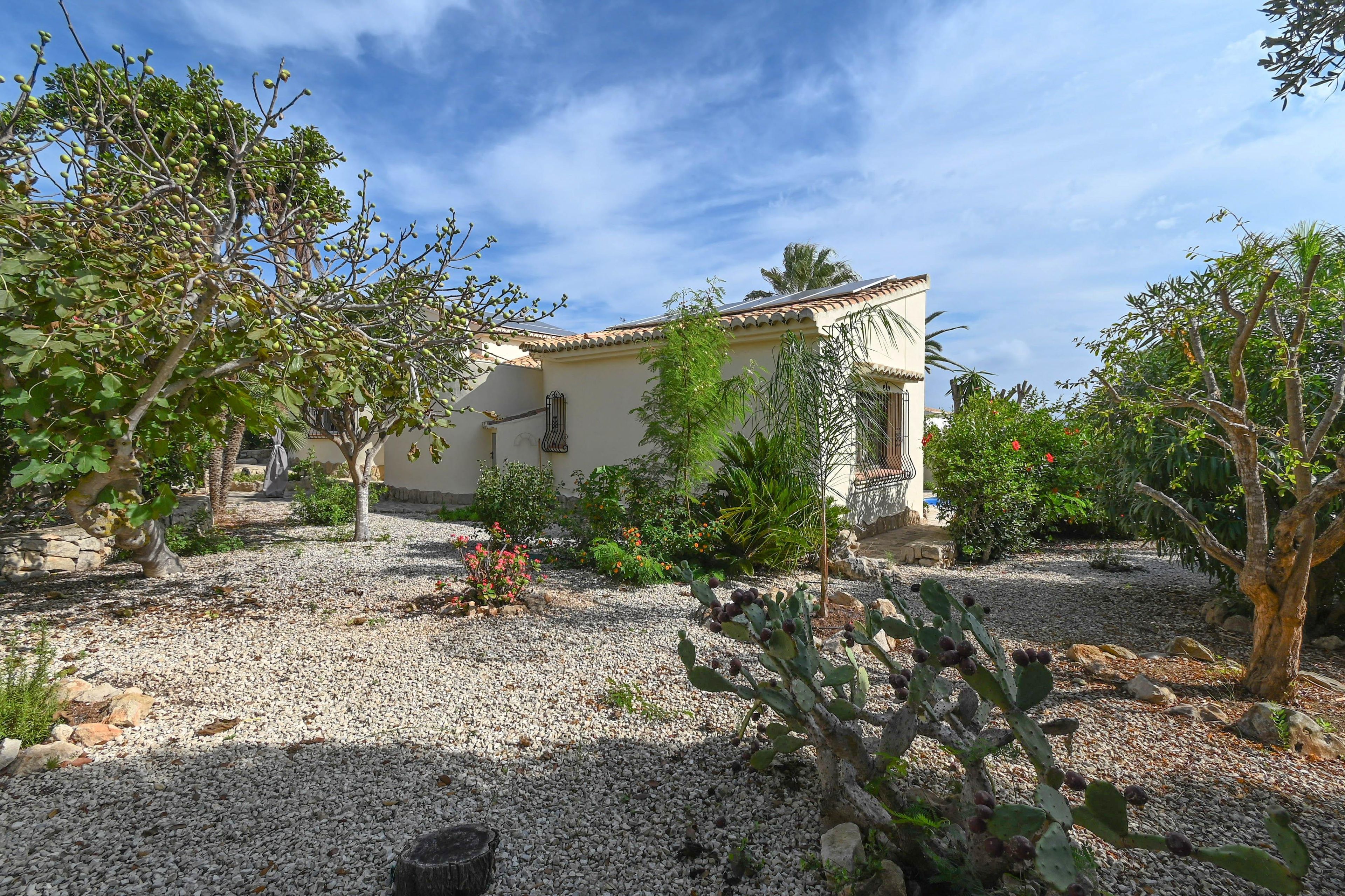 A house with a tiled roof, surrounded by gravel, cacti, and various shrubs.