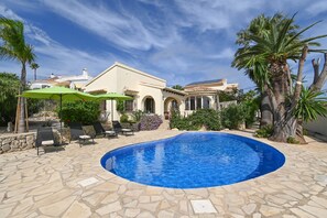 A pool area with a clear blue pool, stone flooring, and outdoor seating with umbrellas.