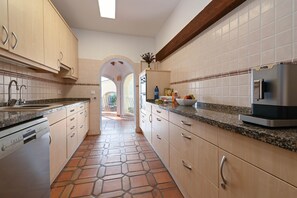 A kitchen with a stone-tiled floor, wooden cabinets, a built-in oven, and a stainless steel refrigerator.
