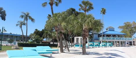 A beachside hotel with lounge chairs, palm trees, and a building with a blue roof.