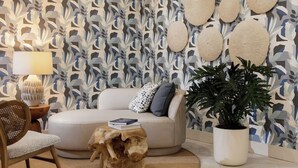 Ein Wohnzimmer mit Wandgestaltung, einem runden Couchtisch, einer Couch mit Kissen, einer Topfpflanze und einer Lampe auf einem Beistelltisch.