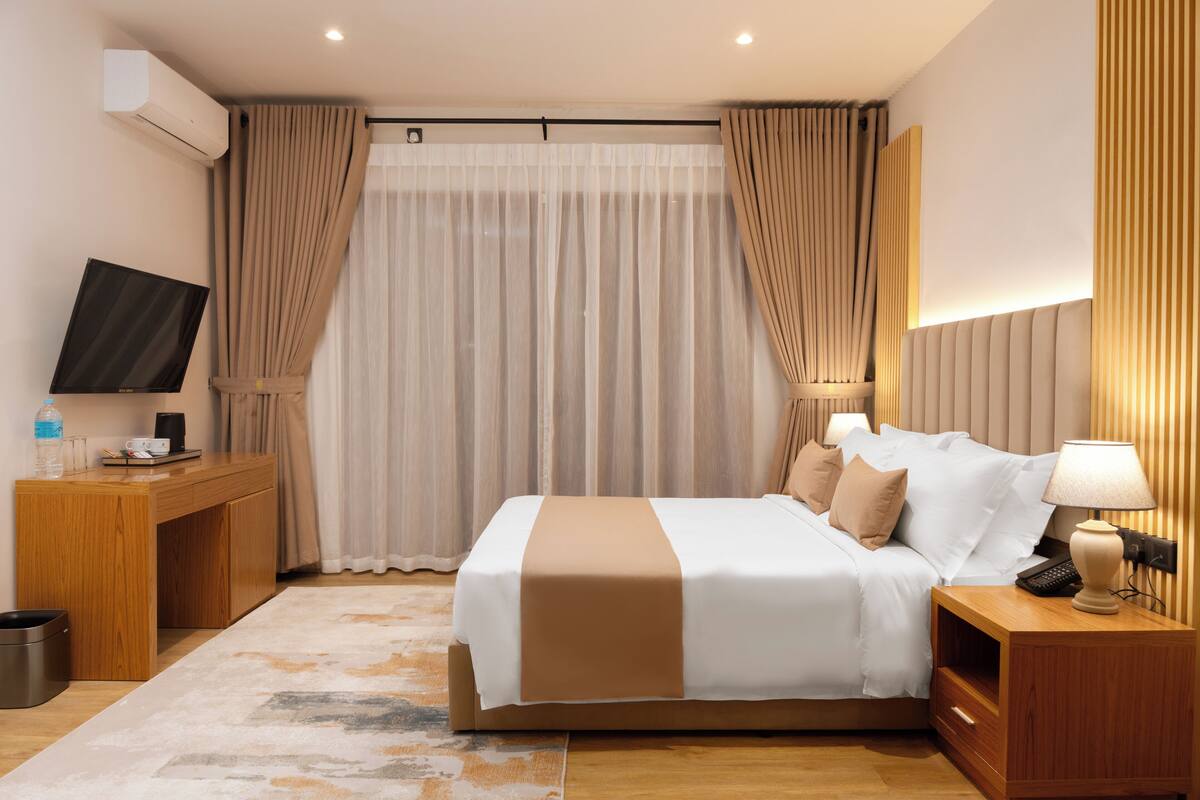 Una habitación de hotel con cama, mesita de noche, lámpara, televisor y cortinas.