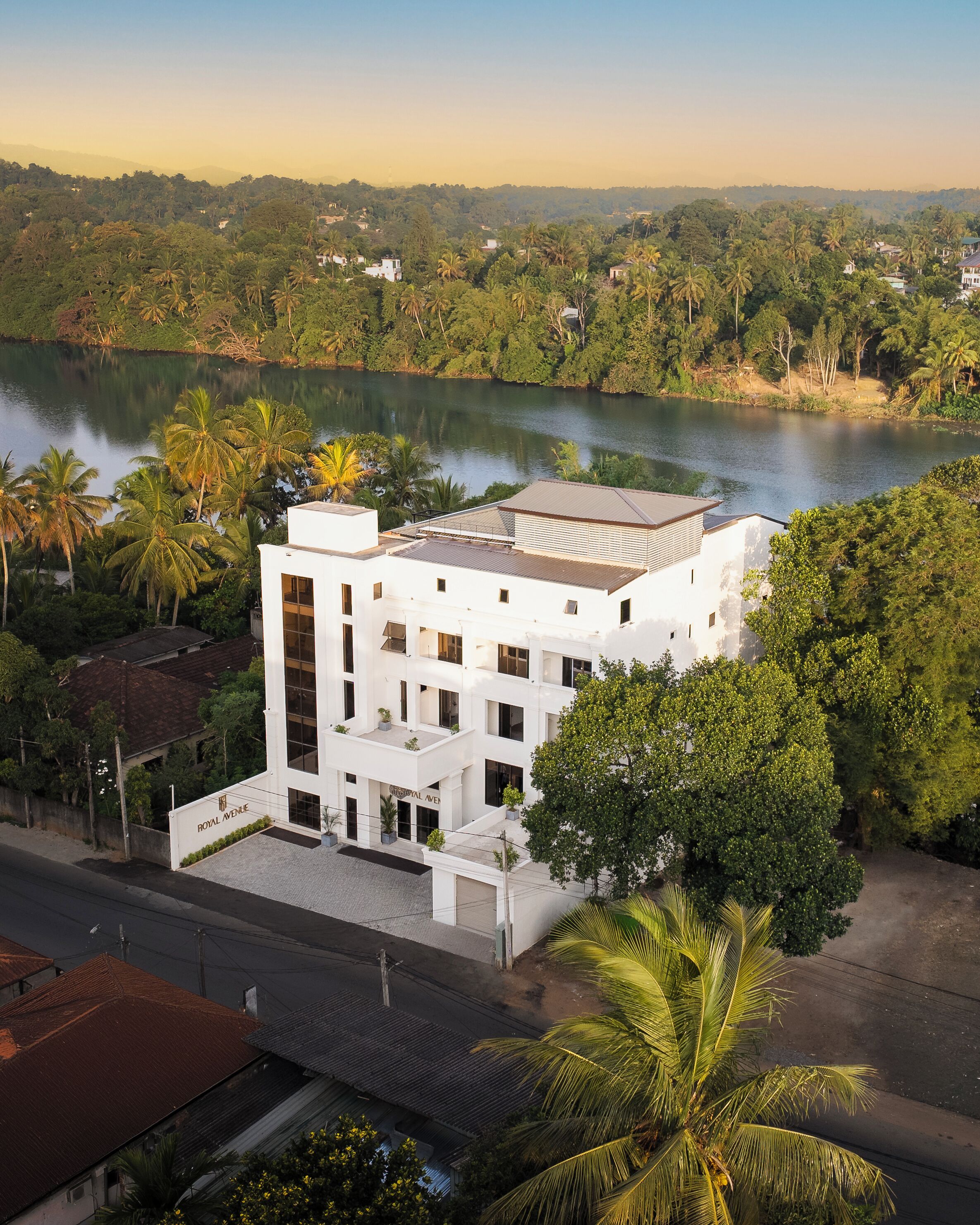 Un bâtiment moderne, de couleur blanche, doté d’un toit plat, situé près d’une étendue d’eau et entouré de verdure.