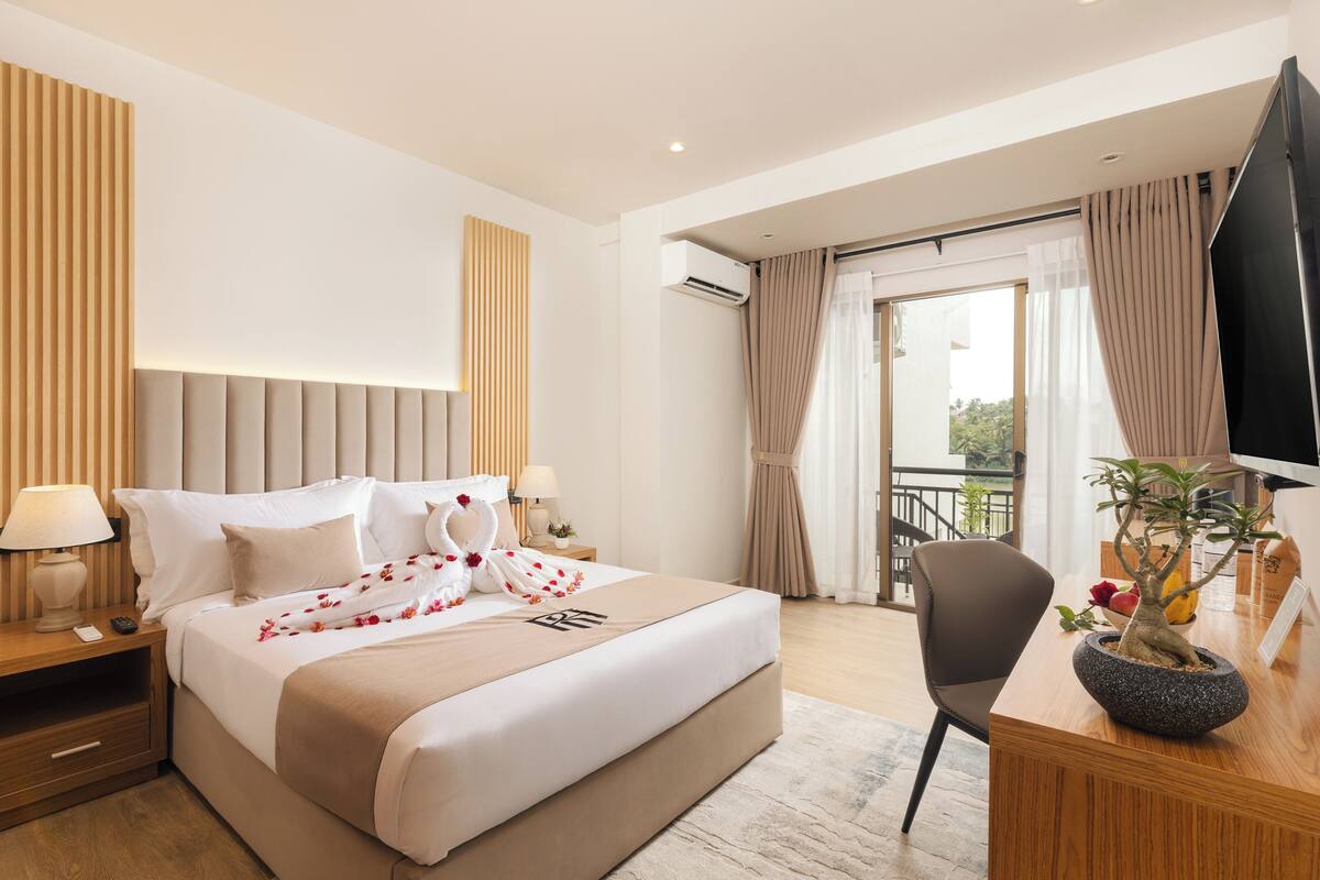 Una habitación de hotel moderna con una cama grande, lámparas de noche, un escritorio con una planta en maceta y vistas al exterior.