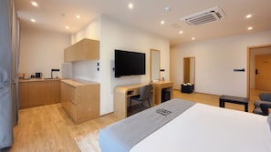 A modern hotel room with a bed, desk, chair, kitchenette, and a TV. - Royal Avenue (Katugastota)