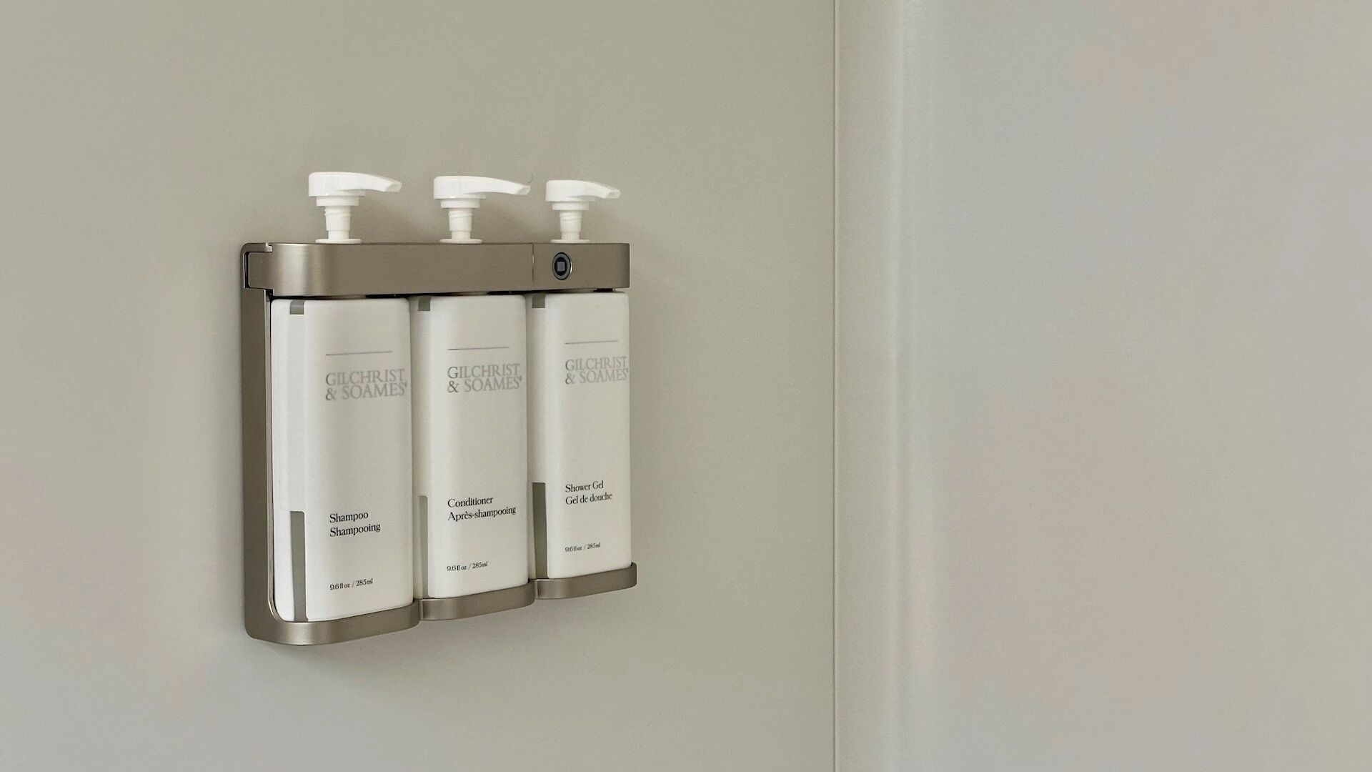 Ein an der Wand befestigter Spender mit drei Flaschen Gilchrist & Soames Shampoo und Conditioner.
