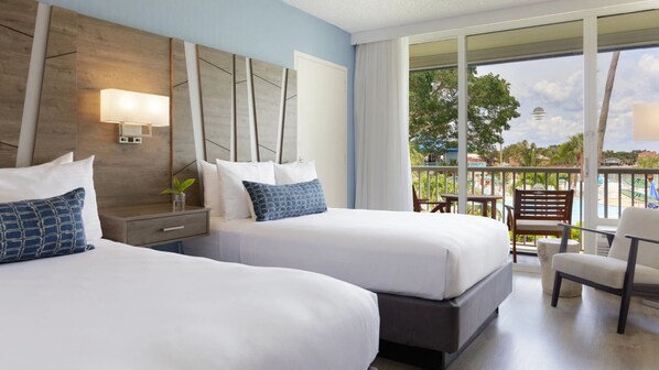 A hotel room with two beds, a nightstand, a lamp, and a view of a pool and palm trees. - Indulge in Coastal Calm | Unit Near Downtown & Local Attractions (St. Petersburg)