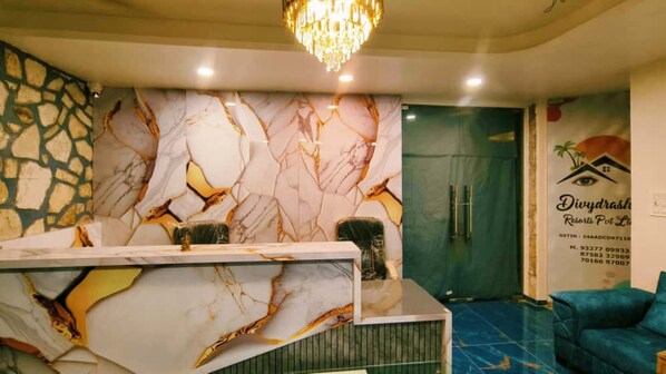 A reception area with a marble wall, a reception desk, a blue sofa, and a chandelier. - Divydrashti Resorts (Waghoriya)