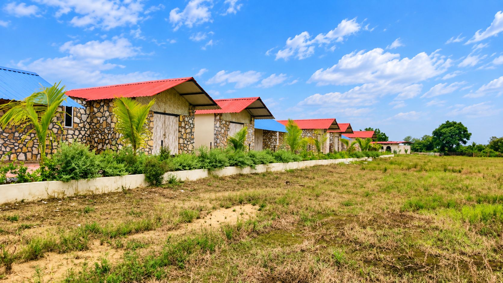 A row of cottages with red roofs, stone walls, and a grassy field in the foreground.