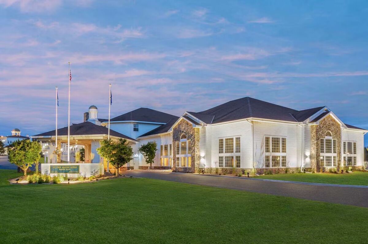A large, multi-story hotel with a central courtyard, flagpoles, and a well-maintained lawn.