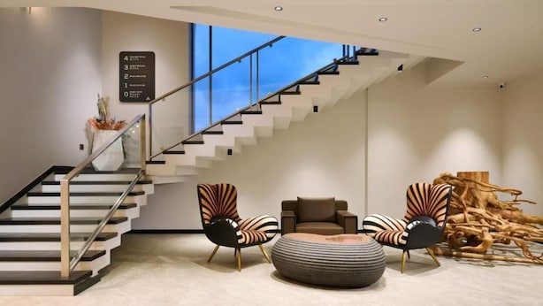 A modern interior with a staircase, two patterned armchairs, a sofa, and a unique wooden sculpture. - GOLDEN CASTLE (Neyyattinkara)