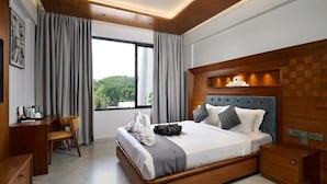 A modern hotel room with a large bed, wooden headboard, and a desk with a chair. - GOLDEN CASTLE (Neyyattinkara)