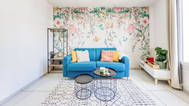A living room with a blue sofa, two round tables, a patterned rug, and a floral wallpaper. - Studio 30s from RER E - Paris in 20 min! (Villemomble)